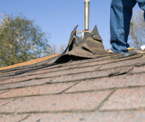 Contractor removing damaged shingles from roof