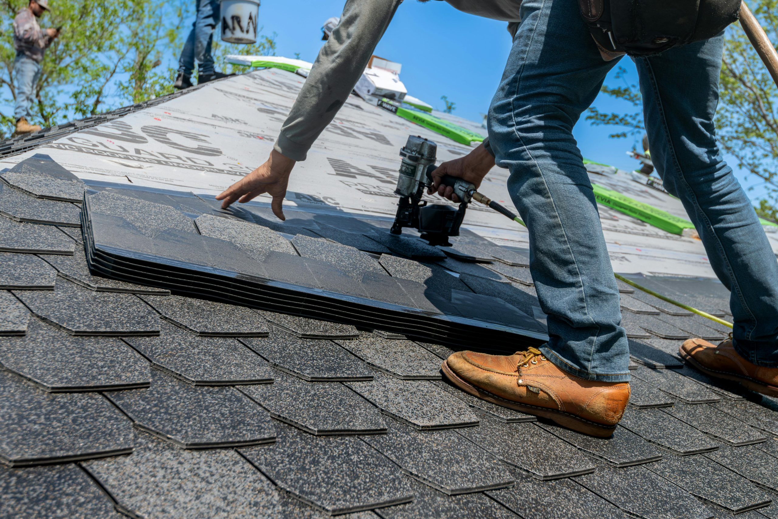 Roofer using nail gun to install roof shingles