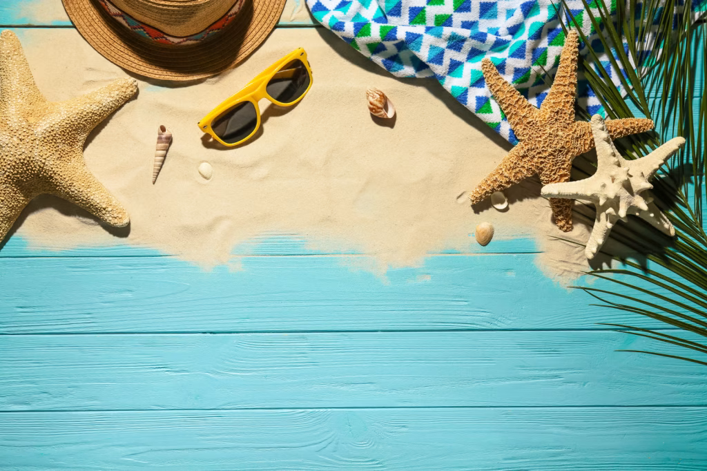 A faux beach scene with sand scattered on blue boards. Yellow sunglasses and shells decorate the sand, giving the image a relaxing, warm appearance--roof replacement summer